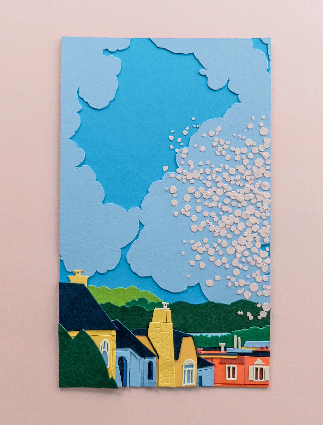 A row of yellow, pale blue, and orange paper houses line the bottom of the artwork. Beyond treelines, puffy blue clouds stretch across the sky, with an explosion of white blossoms flowing over the right side of the piece.