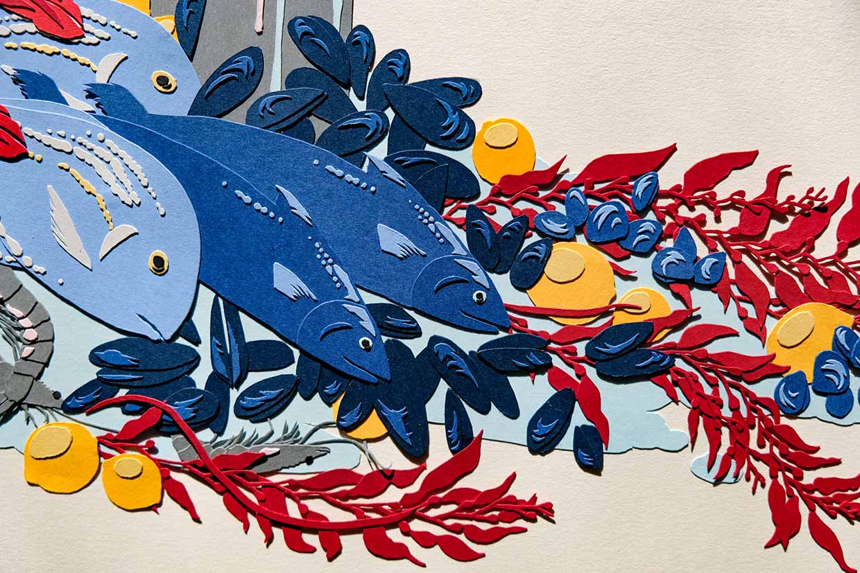 A close up of the artwork shows the details of the fishes' scales, fins, and eyes, as well as the textures of the seaweed and shellfish.