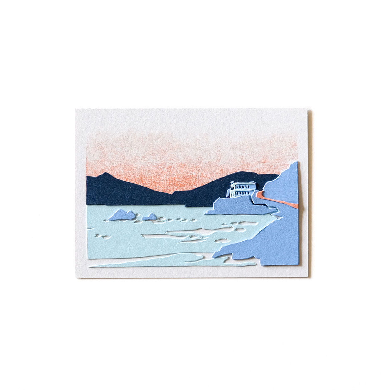 A small piece of cut paper artwork depicts a strip of Ocean Beach bordered by blue cliffs on the right and the ocean to the left, with the Cliff House in the distance.