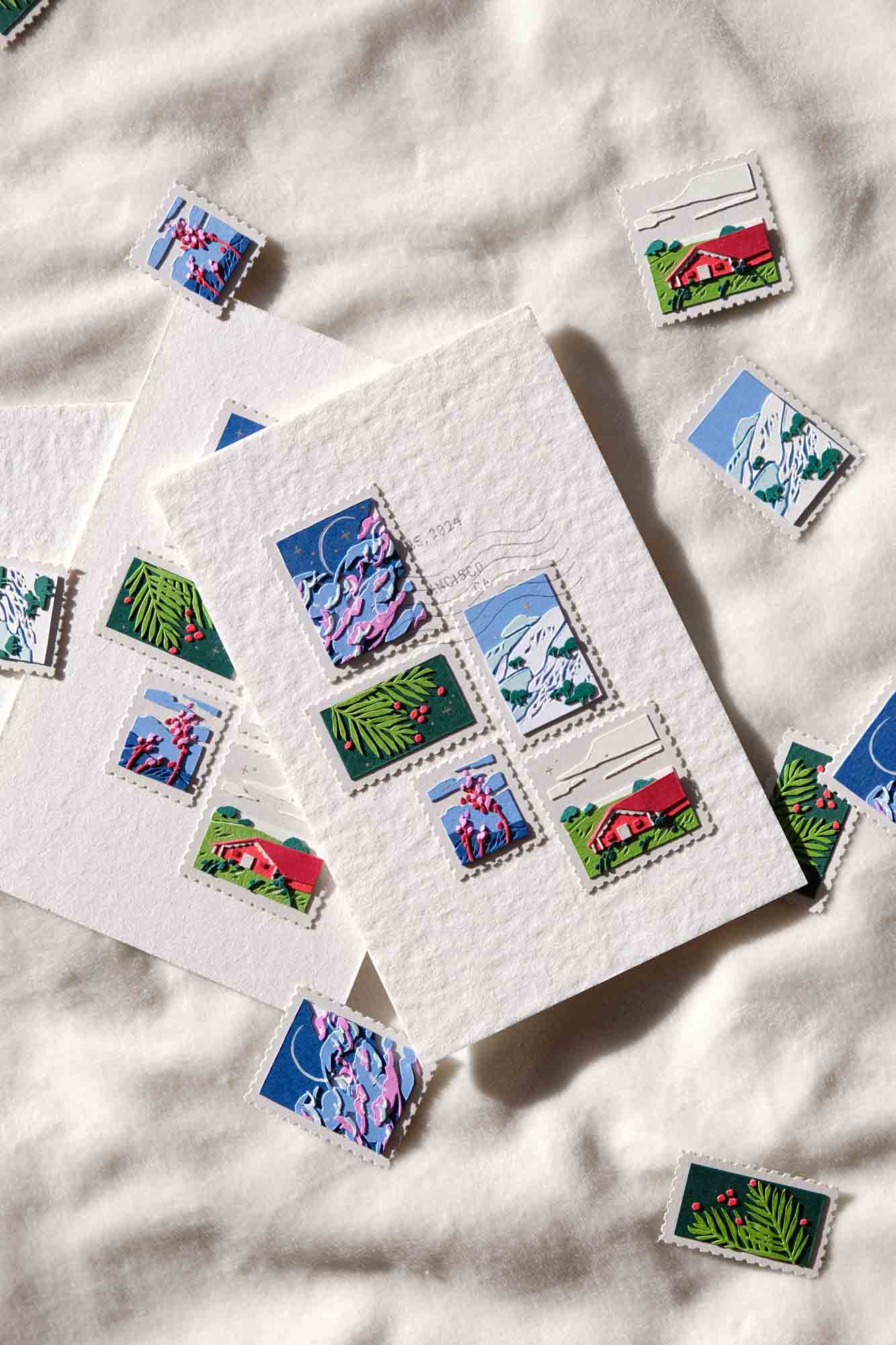 Two holiday cards, each decorated with paper stamps depicting scenes of San Francisco, sit on a snow-like surface, surrounded by additional paper stamps.