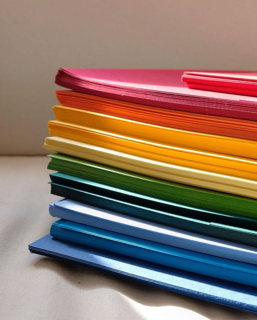 A stack of colored papers sits under a shaft of sunlight against a white backdrop.