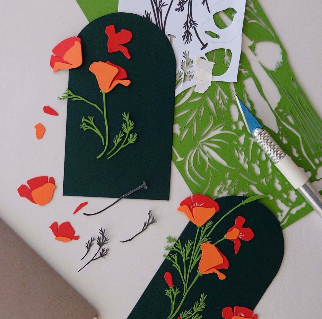 Two sets of unfinished flower compositions are scattered on a table with paper offcuts, a hobby knife, and bits of templates.