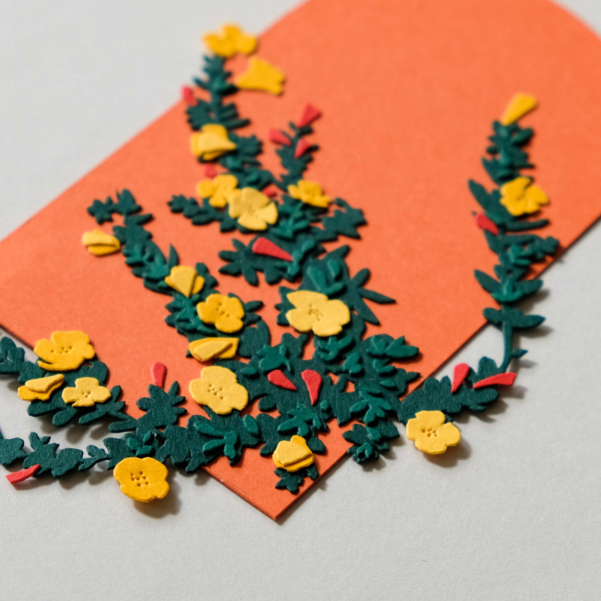 A paper beach primrose plant with yellow flowers sits on an arched orange background.