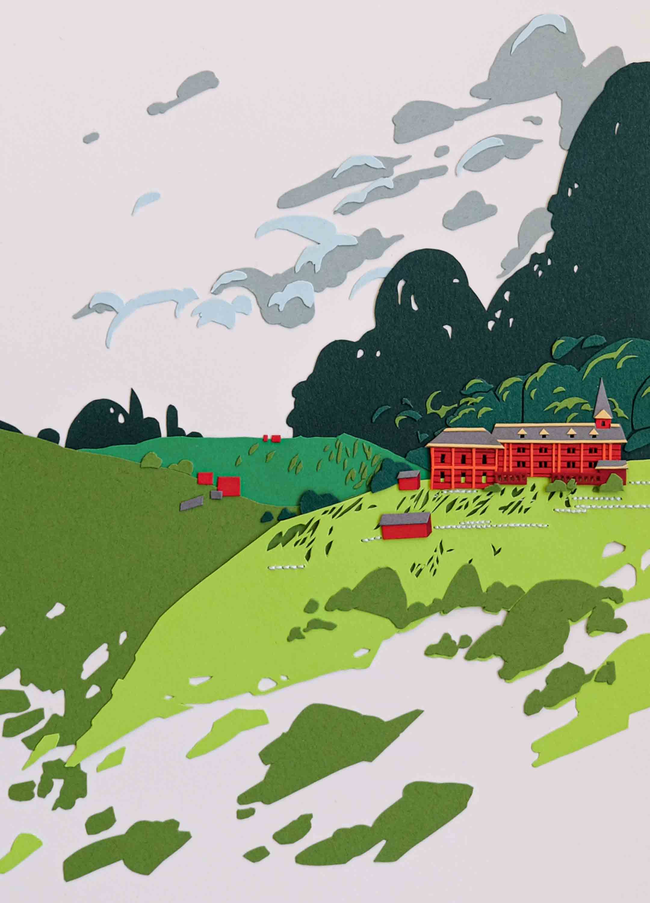 A red paper schoolhouse is surrounded by trees on green hills.