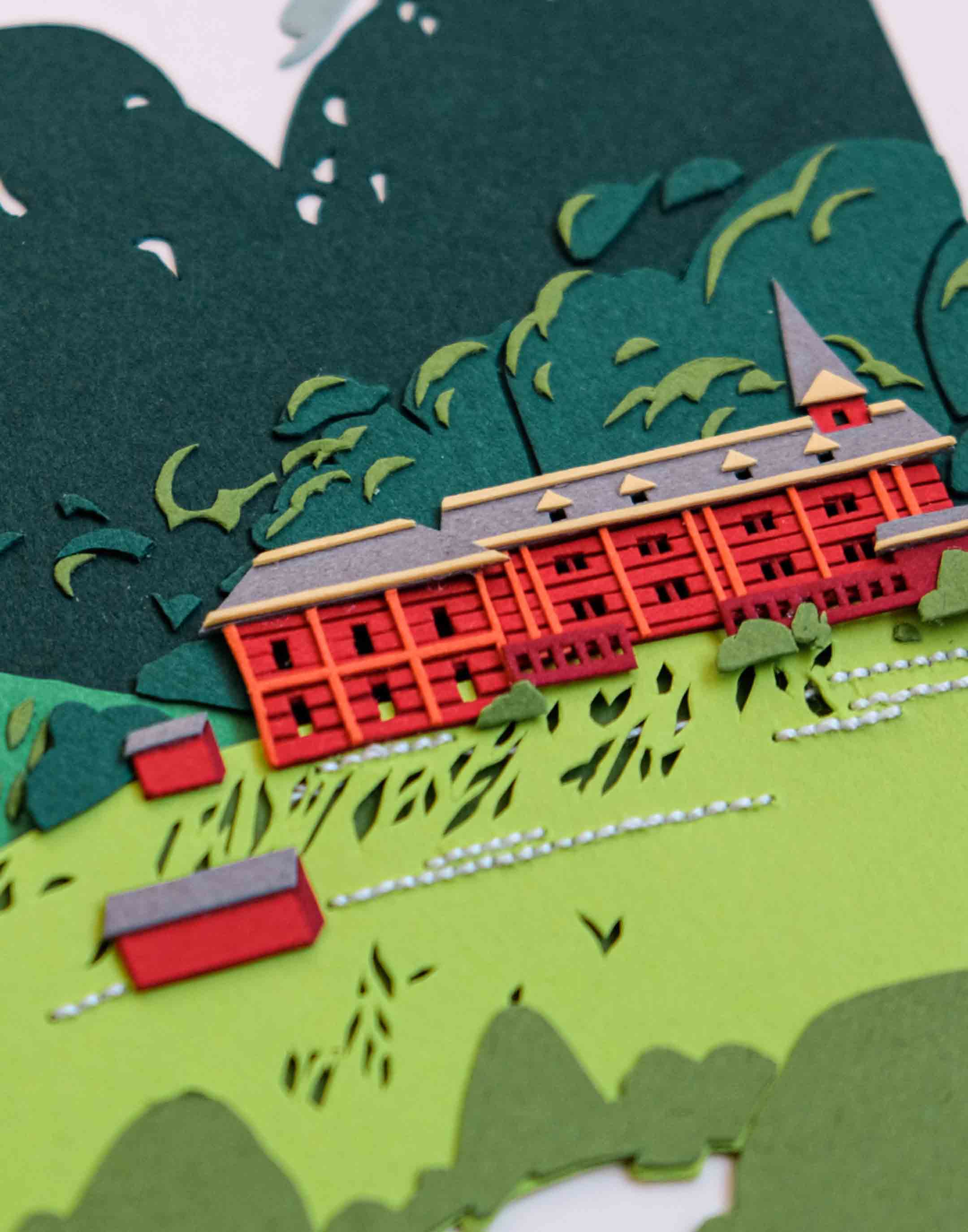 An angled close-up of the artwork reveals the layers of paper that make up the red paper schoolhouse, as well as some white thread details.